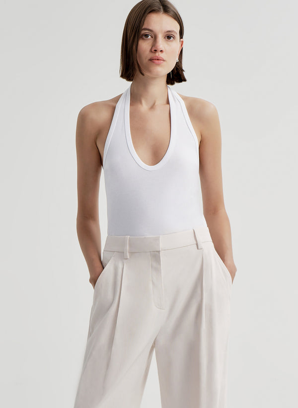 Woman wearing a white halter top and light-colored pants on a plain background