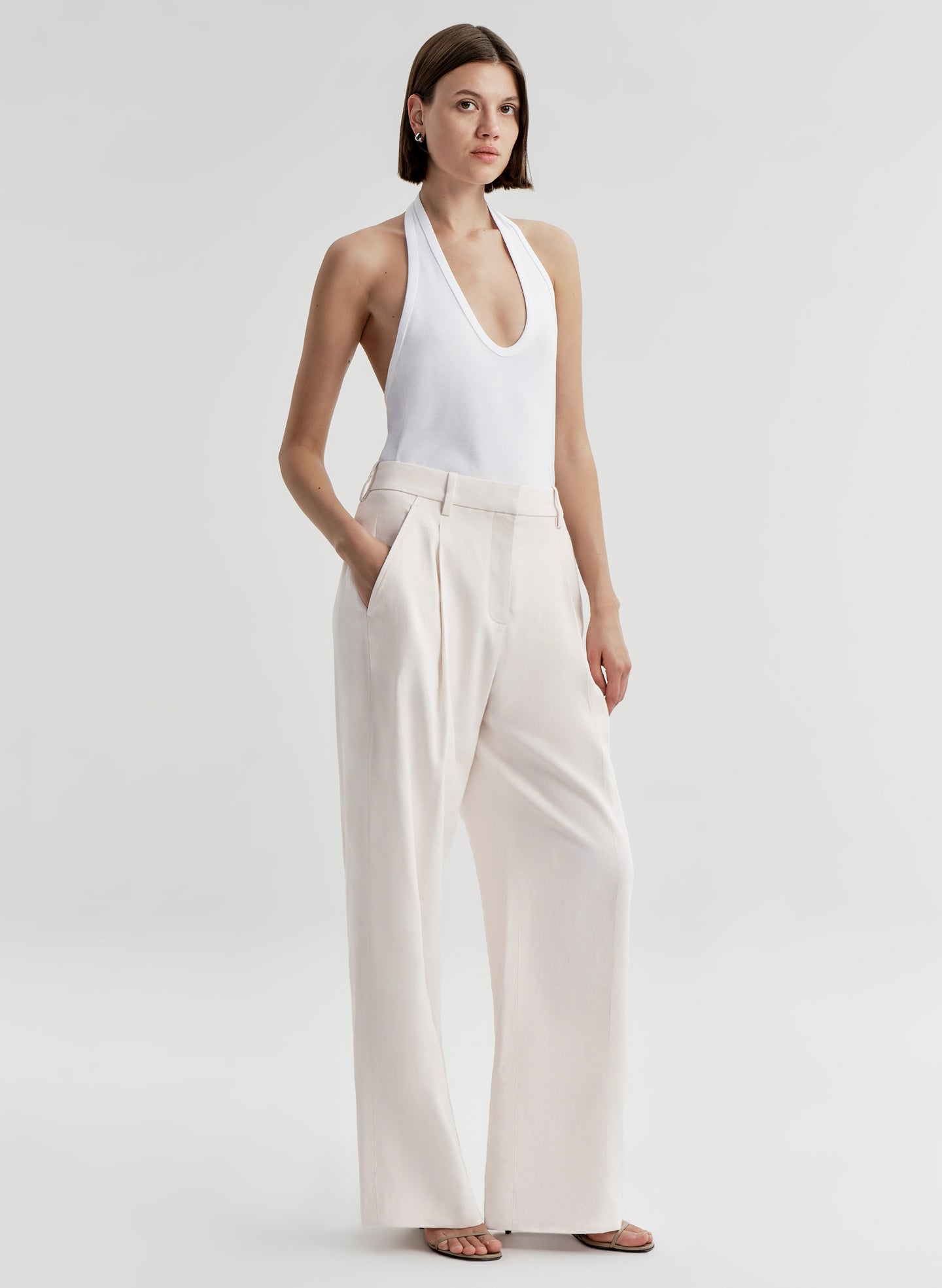 Woman wearing a white halter top and light-colored pants on a plain background