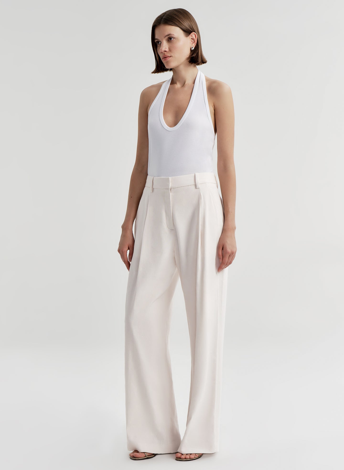 Woman wearing a white halter top and light-colored pants on a plain background