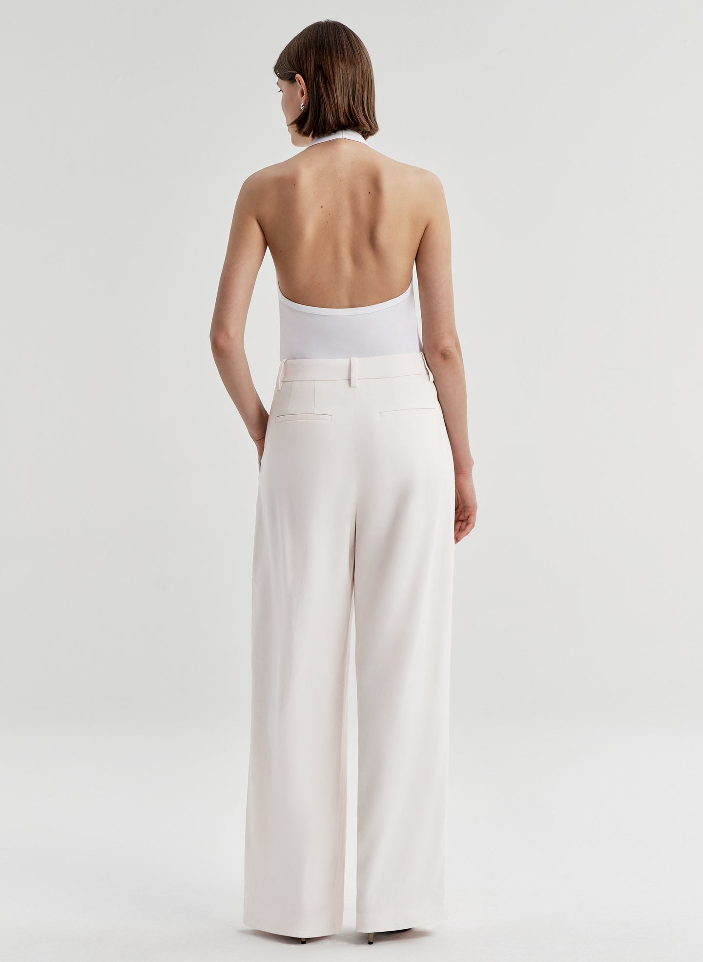 Woman wearing a white halter top and light-colored pants on a plain background