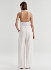 Woman wearing a white halter top and light-colored pants on a plain background