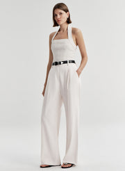Woman wearing a cream colored halter top with a black belt with white pants and a light gray background