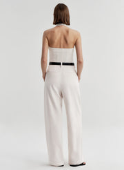 Woman wearing a cream colored halter top with a black belt with white pants and a light gray background