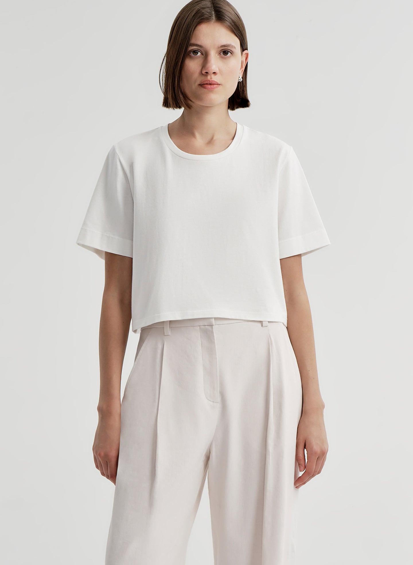Woman wearing a white t-shirt and light-colored pants with a plain background