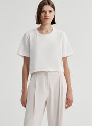 Woman wearing a white t-shirt and light-colored pants with a plain background