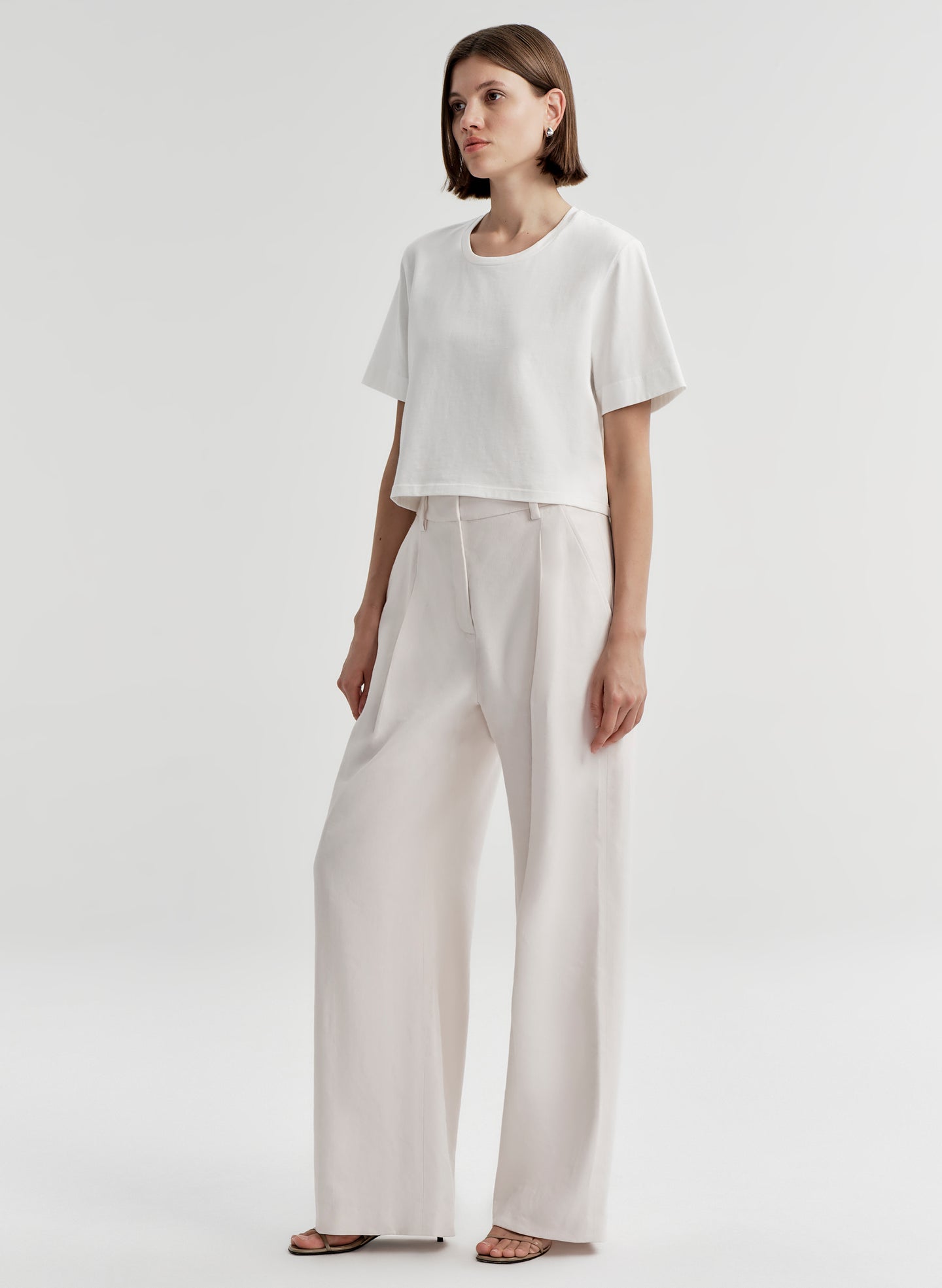 Woman wearing a white t-shirt and light-colored pants with a plain background