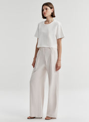 Woman wearing a white t-shirt and light-colored pants with a plain background