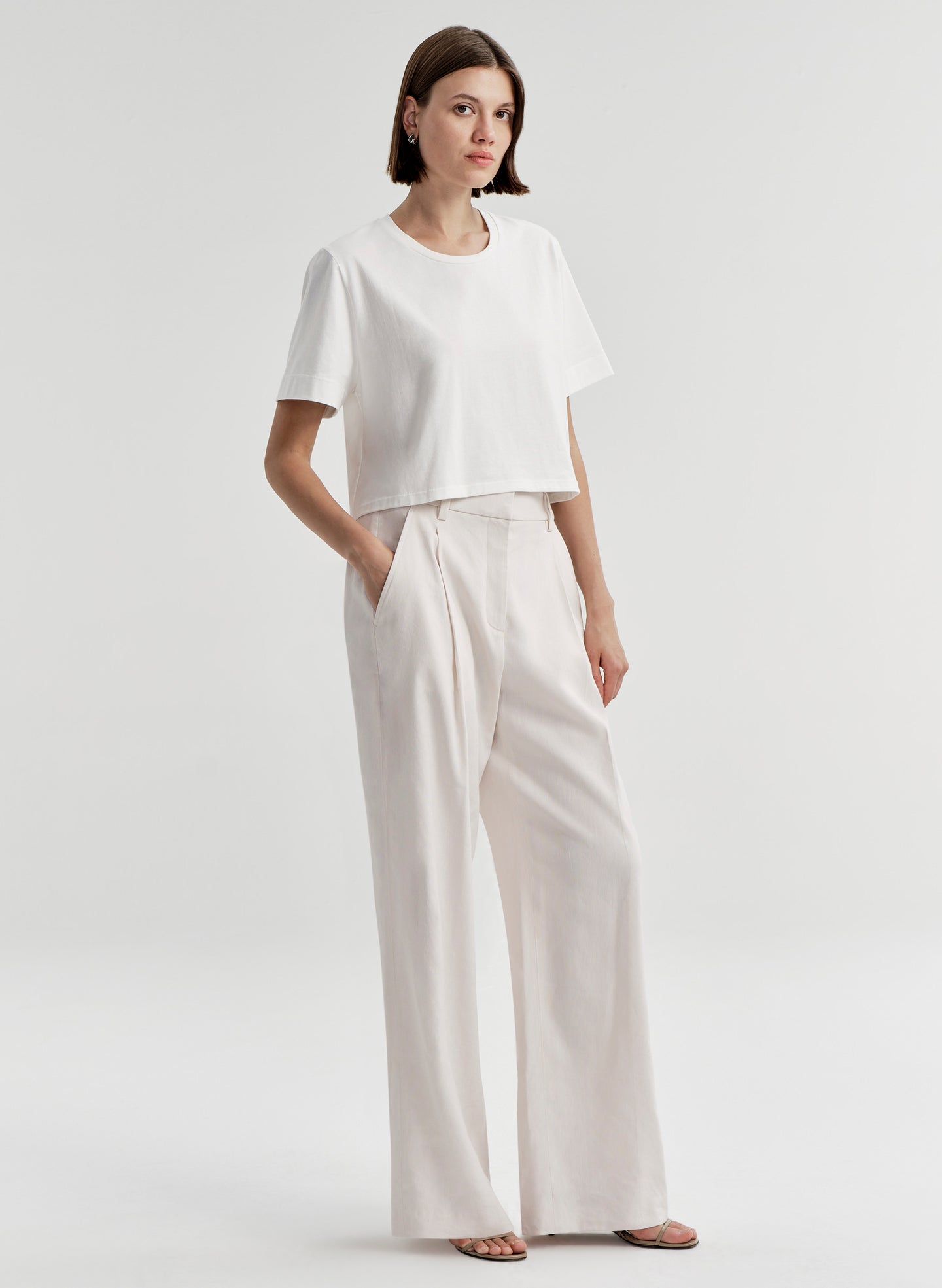 Woman wearing a white t-shirt and light-colored pants with a plain background