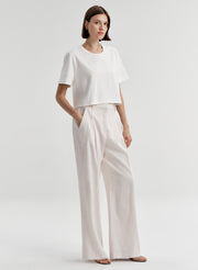 Woman wearing a white t-shirt and light-colored pants with a plain background