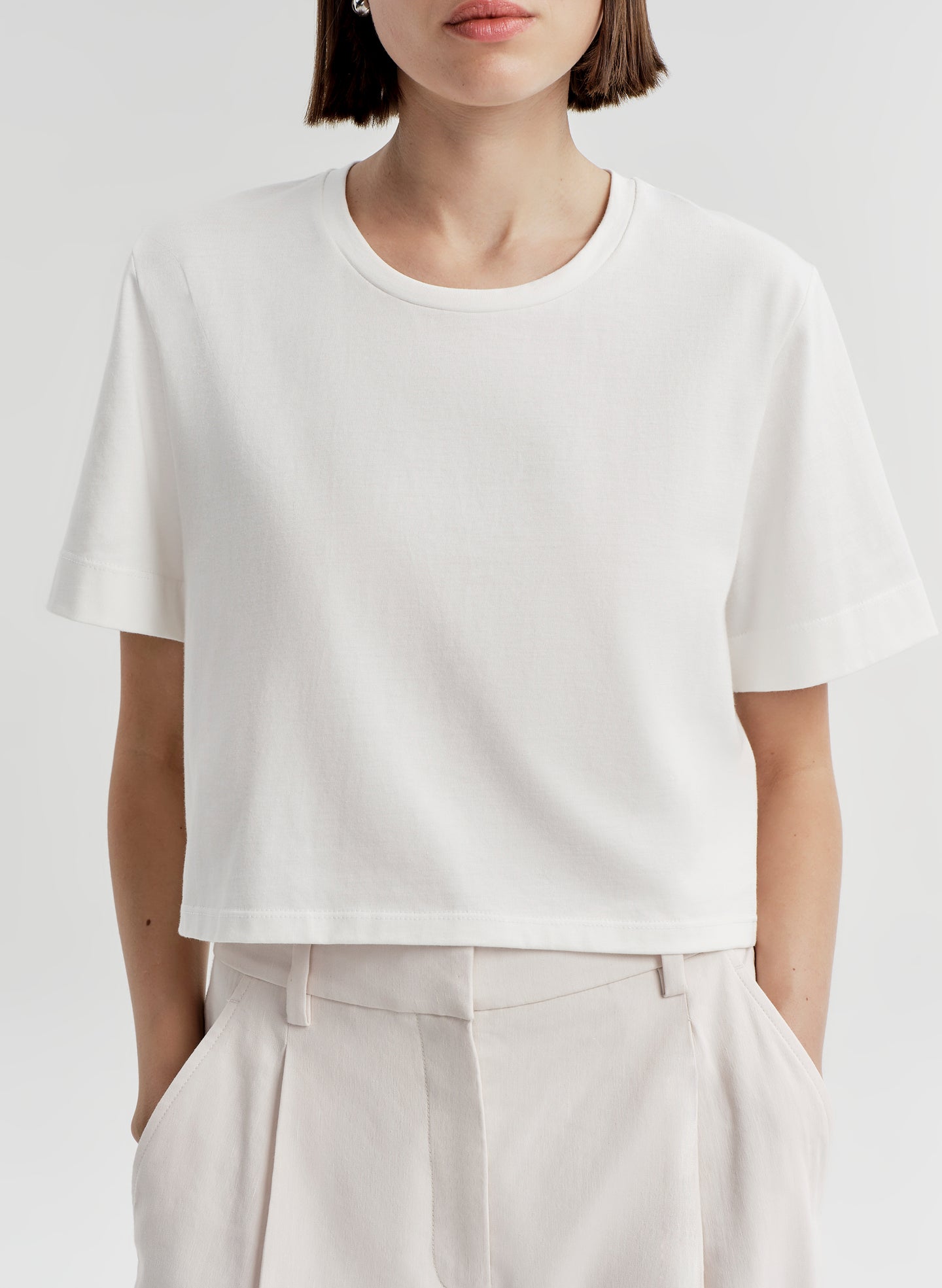 Woman wearing a white t-shirt and light-colored pants with a plain background