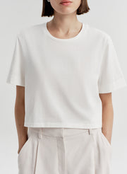 Woman wearing a white t-shirt and light-colored pants with a plain background