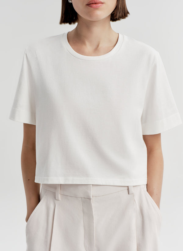 Woman wearing a white t-shirt and light-colored pants with a plain background