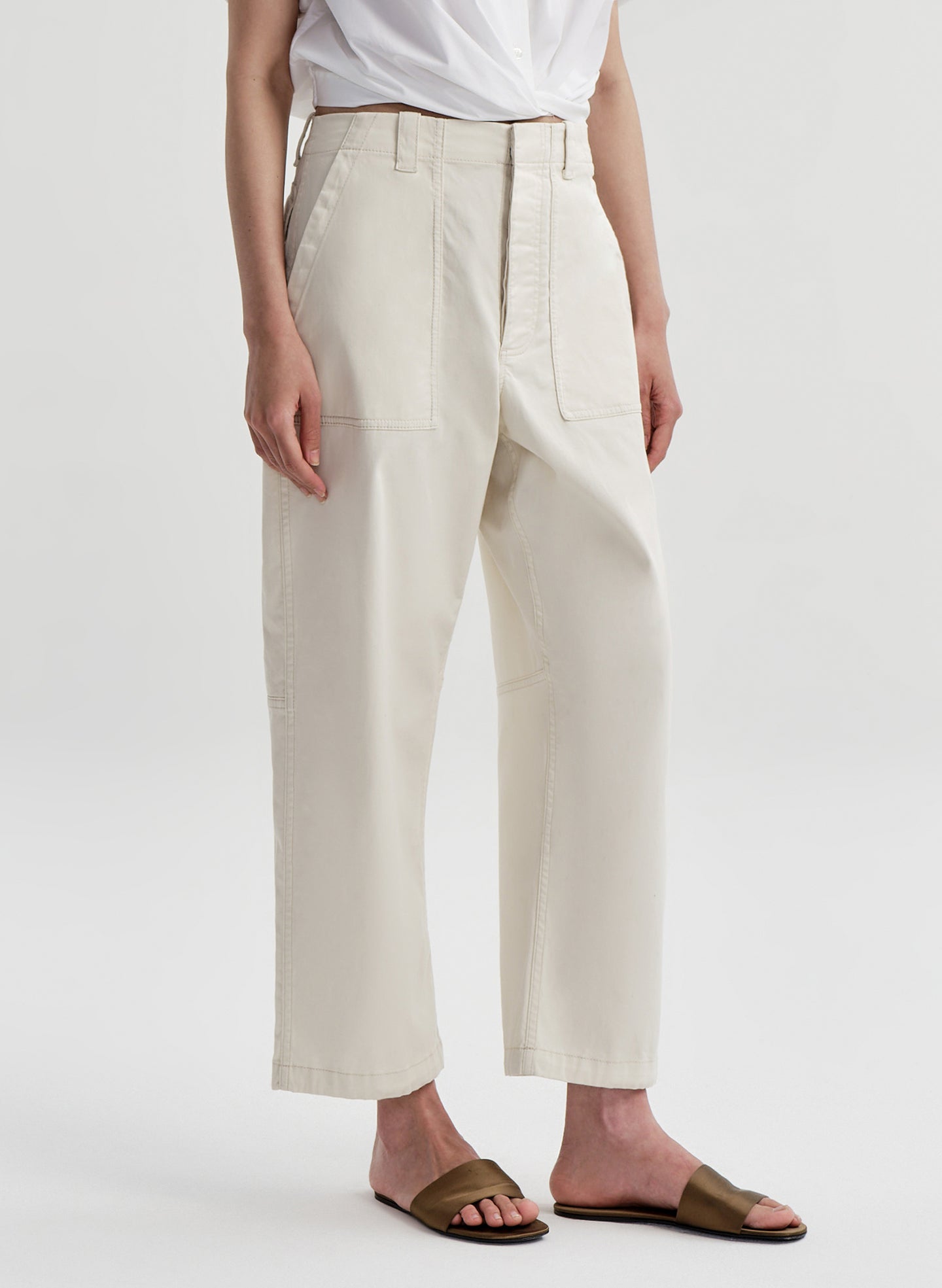 Woman wearing beige twill pants and a white top on a white background