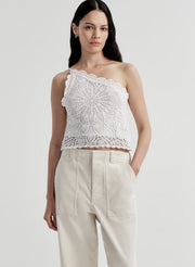 Woman wearing a white crochet one-shoulder top and beige pants on a light gray background