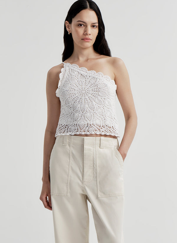 Woman wearing a white crochet one-shoulder top and beige pants on a light gray background