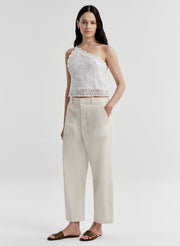 Woman wearing a white crochet one-shoulder top and beige pants on a light gray background