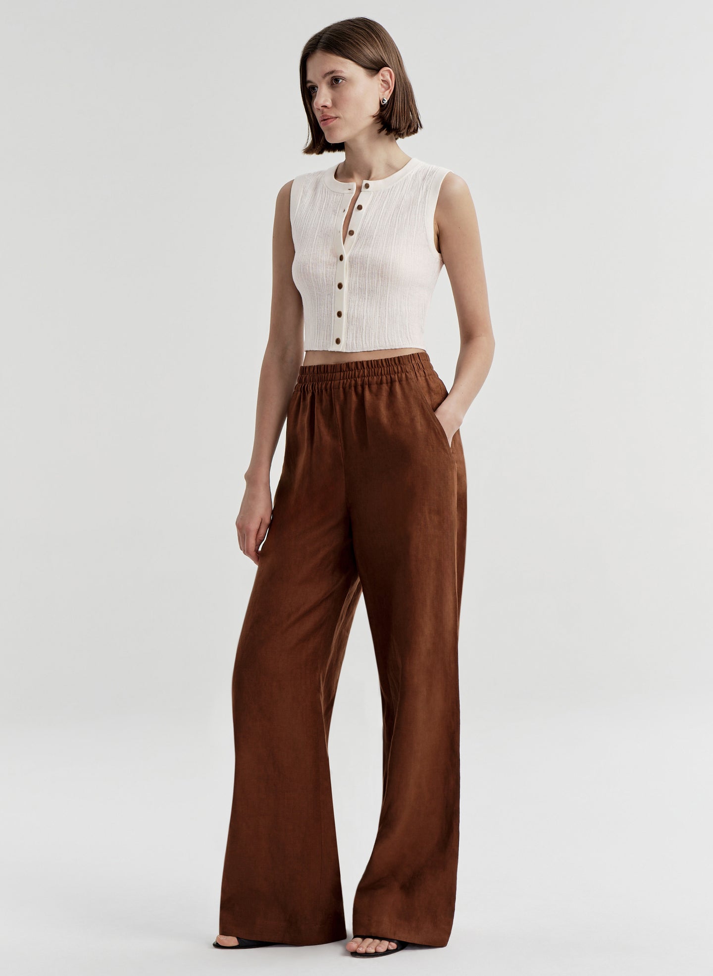 Woman wearing a white sleeveless top and brown wide-leg pants on a white background