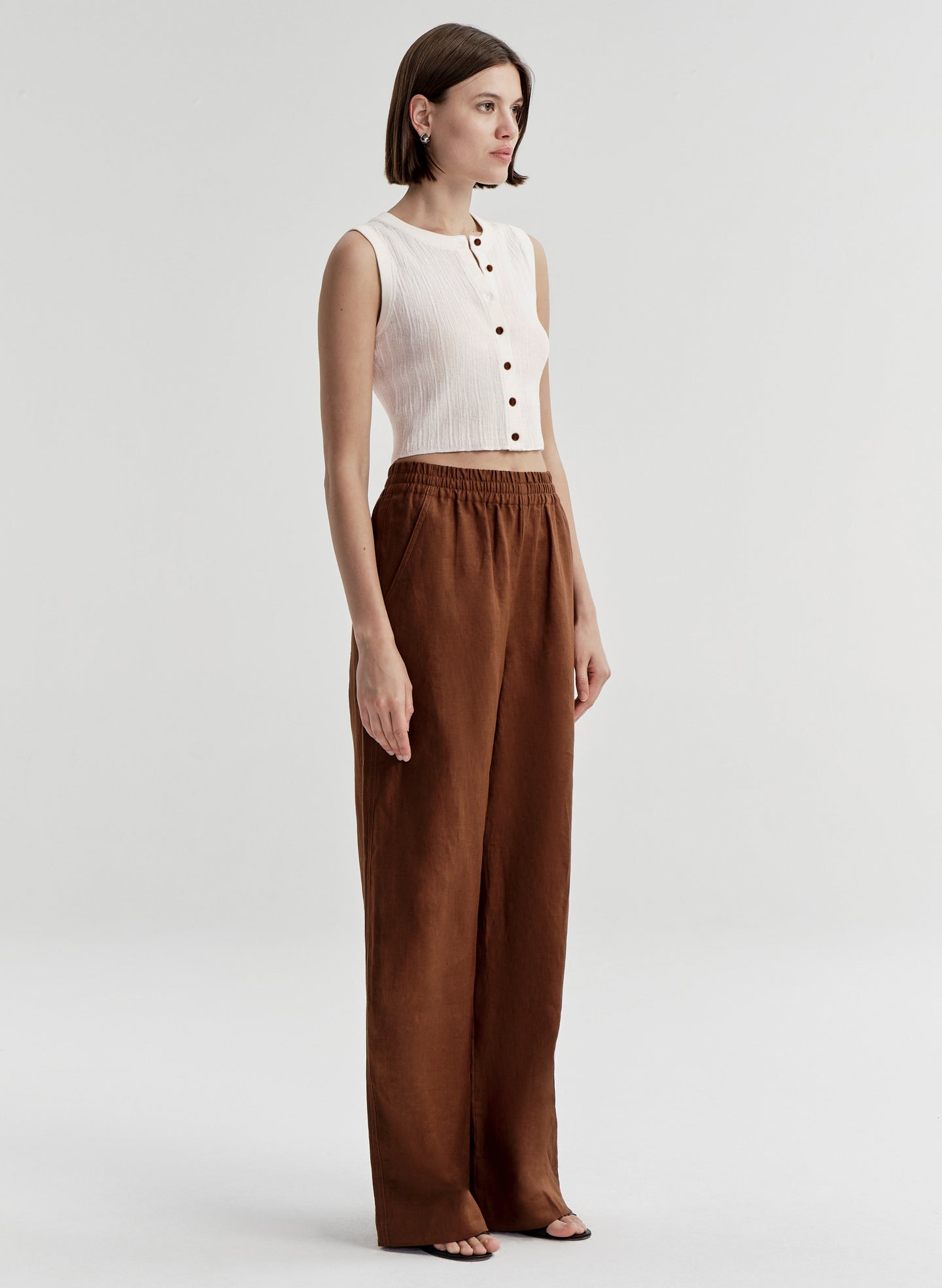 Woman wearing a white sleeveless top and brown wide-leg pants on a light gray background