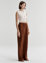 Woman wearing a white sleeveless top and brown wide-leg pants on a light gray background