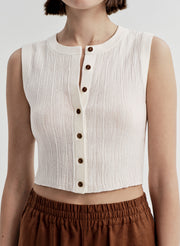 White sleeveless top with brown buttons worn by a person on a white background