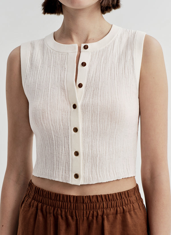 White sleeveless top with brown buttons worn by a person on a white background