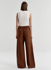 Woman wearing a white sleeveless top and brown wide-leg pants on a white background