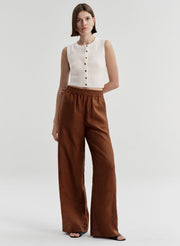 Woman wearing a white sleeveless top and brown wide-leg pants on a light gray background