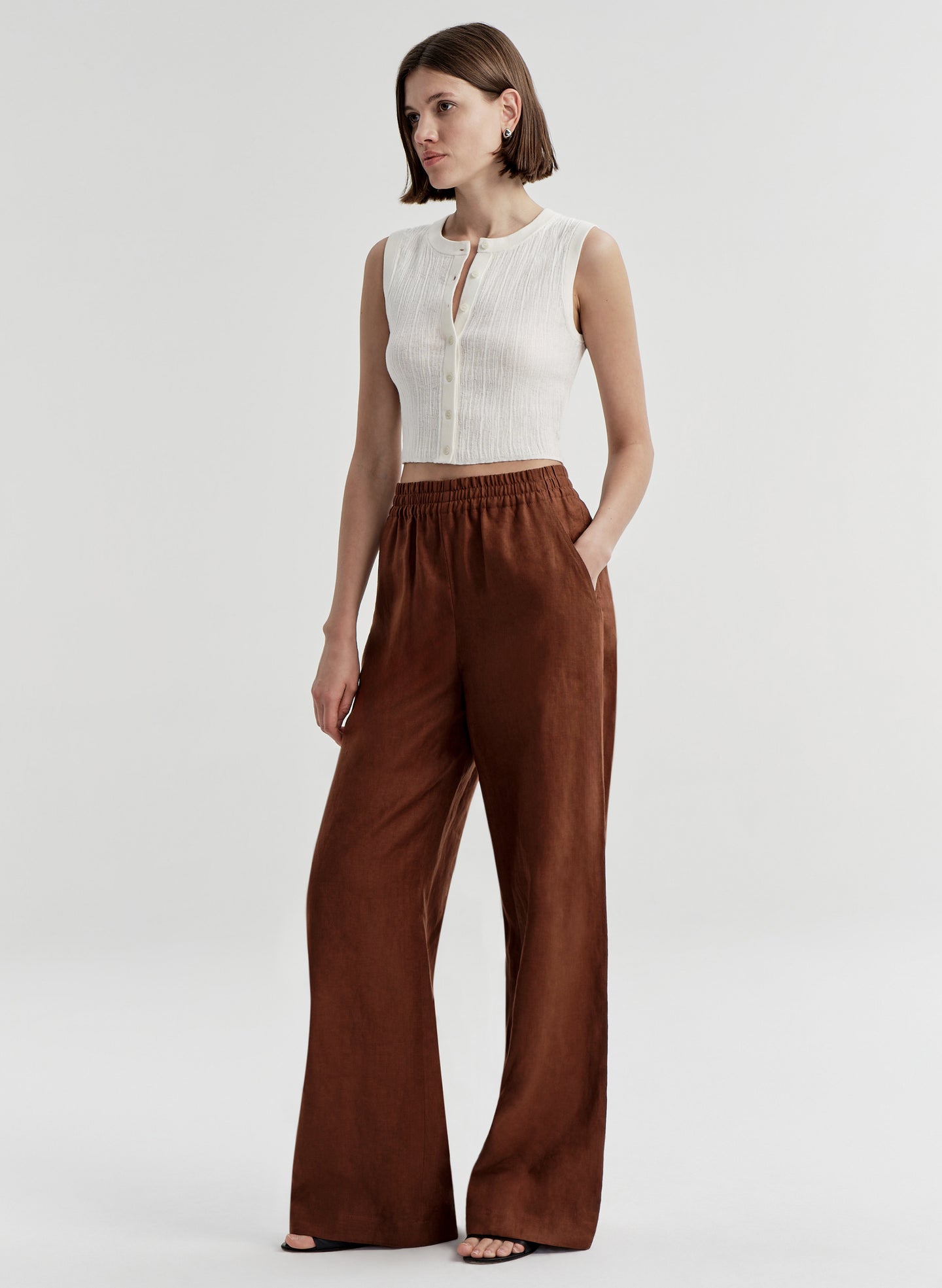 Woman wearing brown linen pants with a white top on a light gray background
