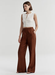 Woman wearing brown linen pants with a white top on a light gray background