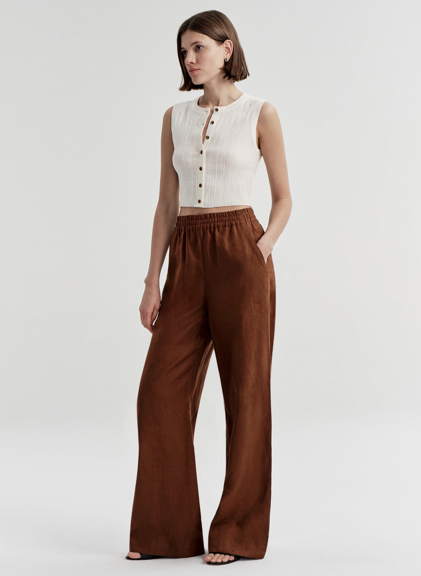 Woman wearing a white sleeveless top and brown wide-leg pants on a white background