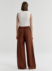 Woman wearing brown linen pants with a white top on a light gray background
