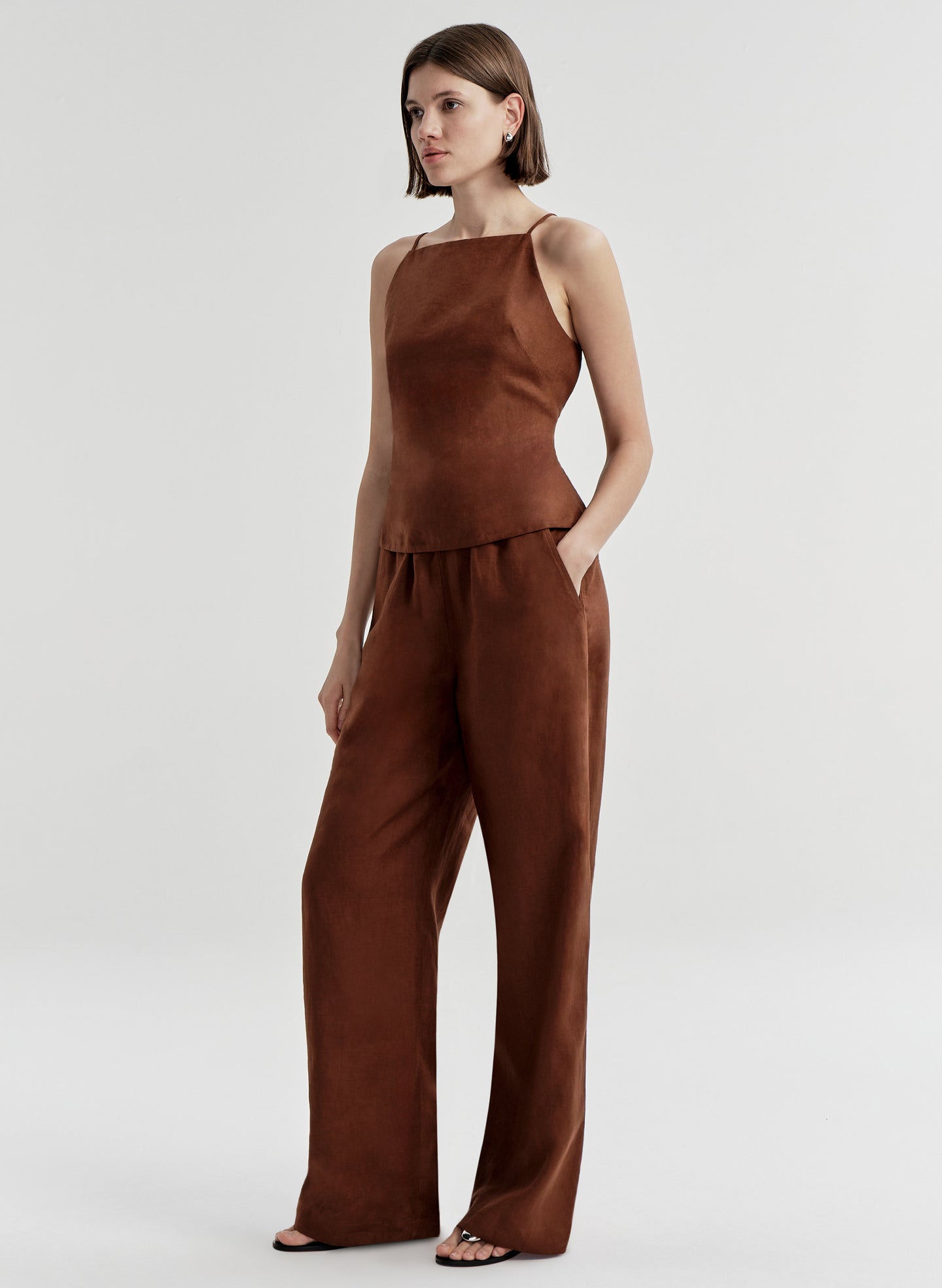 Woman wearing a brown sleeveless top and matching  pants on a light gray background