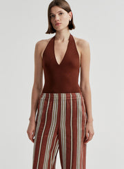 Woman wearing a brown halter top and striped pants on a light gray background