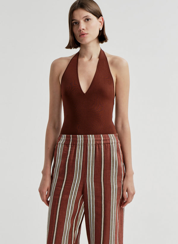 Woman wearing a brown halter top and striped pants on a light gray background