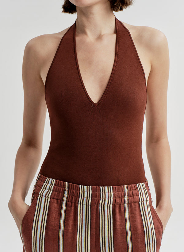 Woman wearing a brown halter top and striped pants on a light gray background