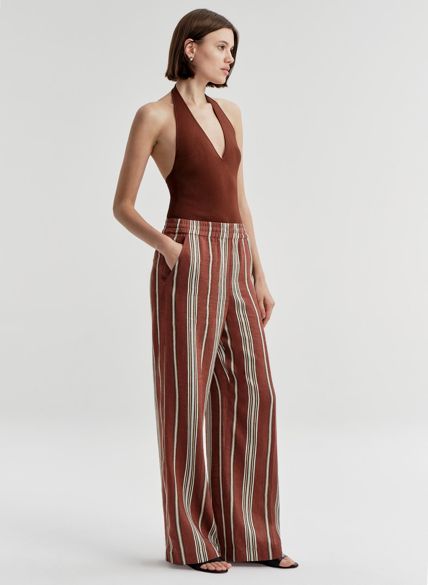 Woman wearing a brown halter top and striped pants on a light gray background