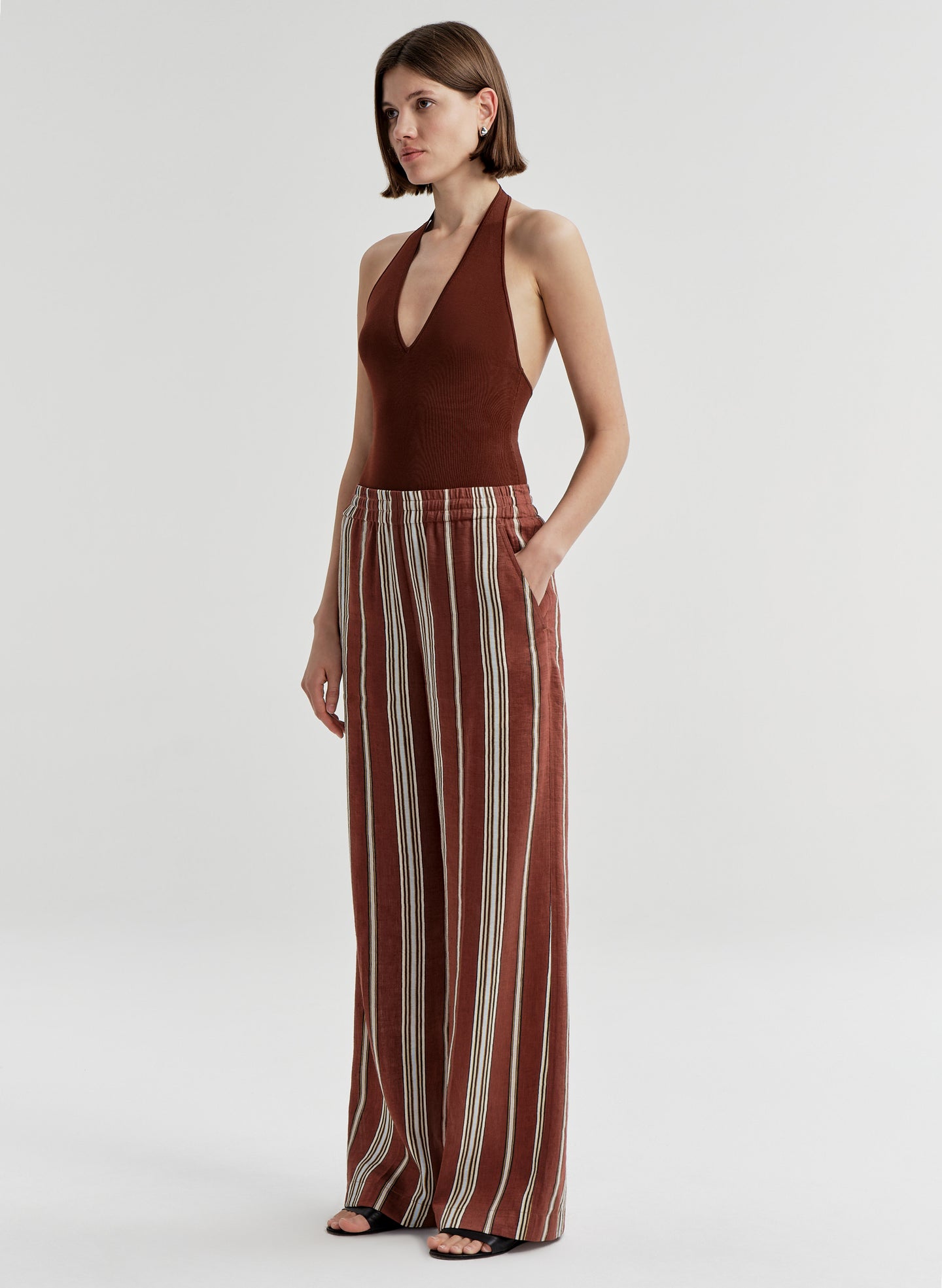 Woman wearing a brown halter top and striped pants on a light gray background