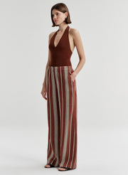 Woman wearing a brown halter top and striped pants on a light gray background