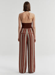 Woman wearing a brown halter top and striped pants on a light gray background