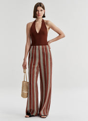 woman wearing brown bodysuit and brown pants, carrying a raffia bag
