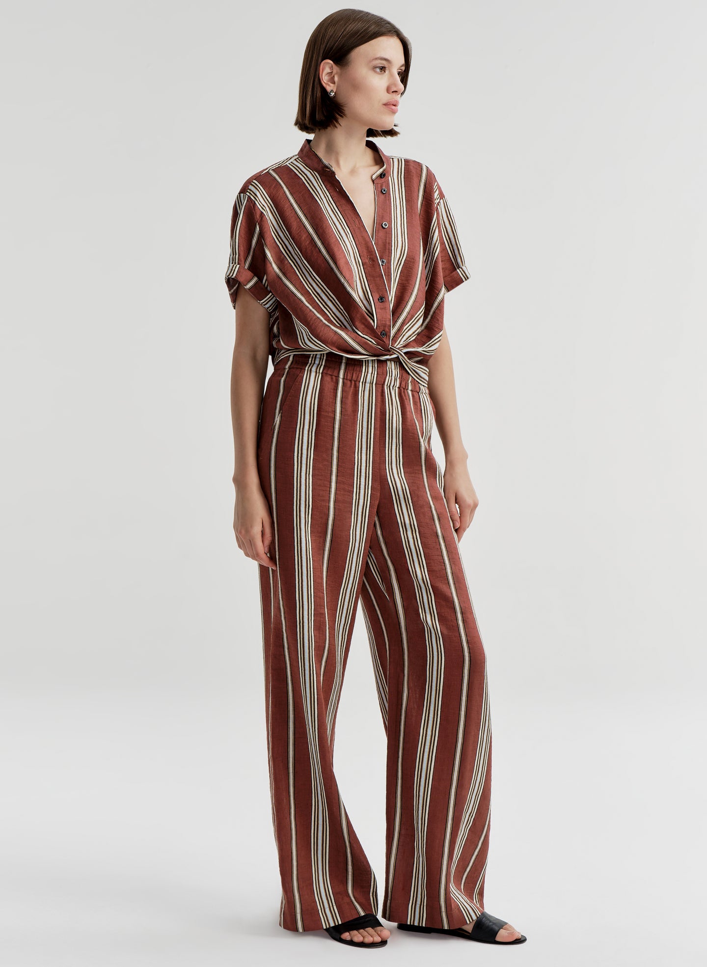 Woman wearing a brown and white striped linen top and matching pants on a plain background