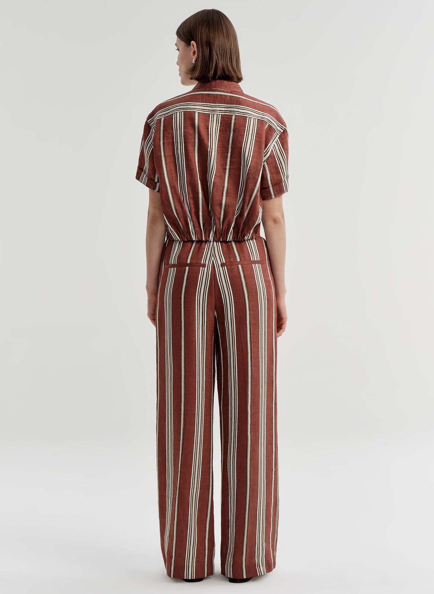 Woman wearing a brown and white striped linen top and matching pants on a plain background