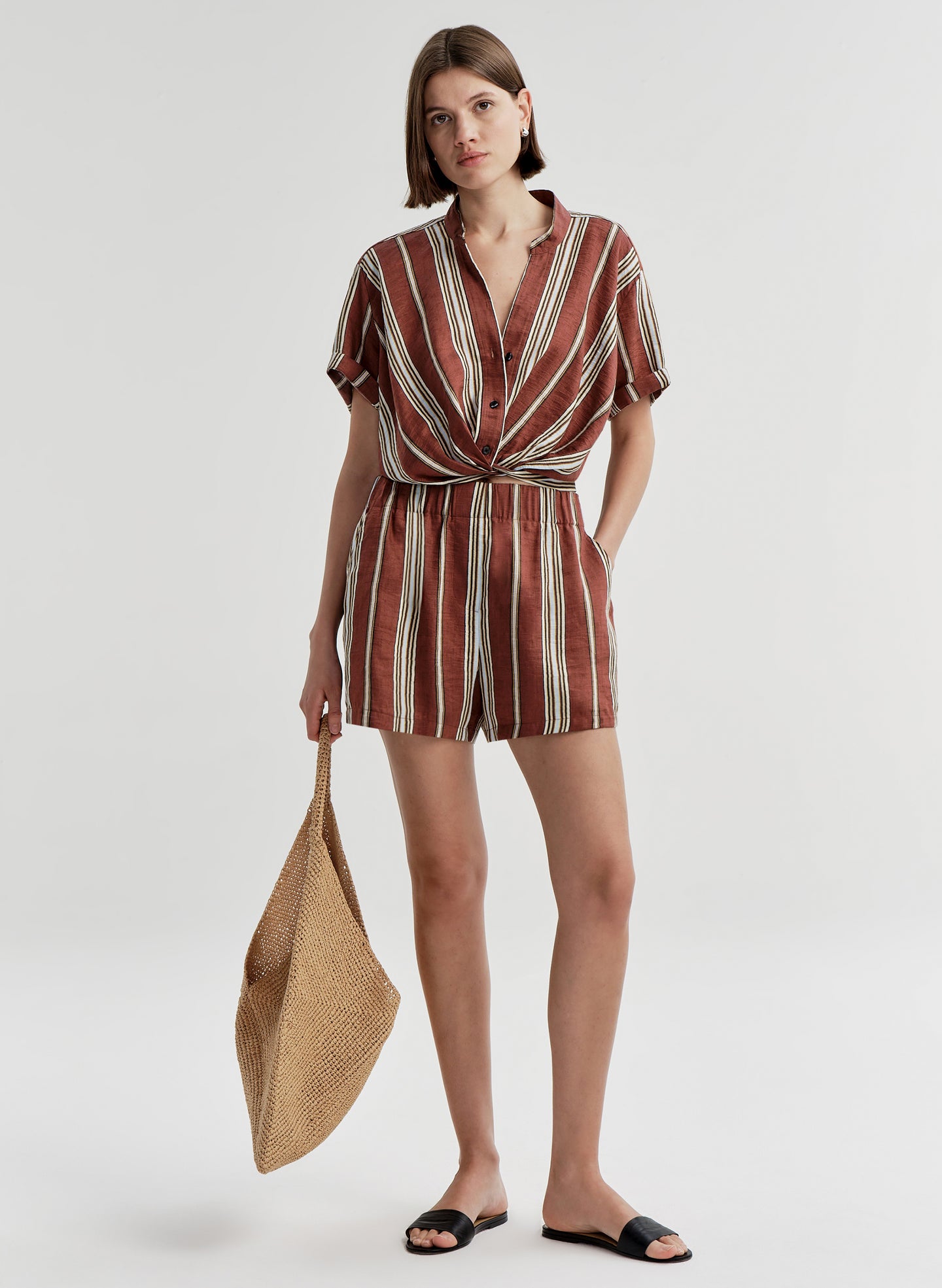 Woman wearing a striped otufit holding a straw bag on a white background