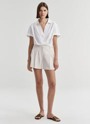 Woman wearing beige linen shorts with a white top on a plain background