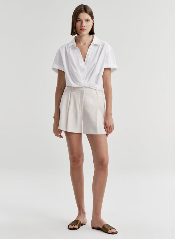 Woman wearing beige linen shorts with a white top on a plain background