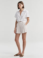 Woman wearing beige linen shorts with a white top on a plain background