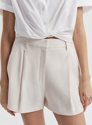 Woman wearing beige linen shorts with a white top on a plain background