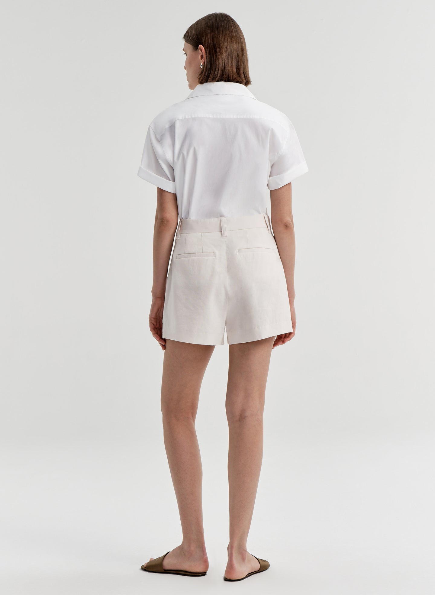 Woman wearing beige linen shorts with a white top on a plain background