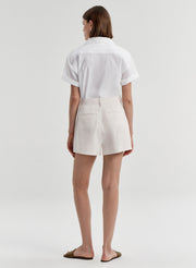 Woman wearing beige linen shorts with a white top on a plain background