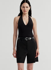 Woman wearing a black halter bodysuit and black shorts on a light gray background